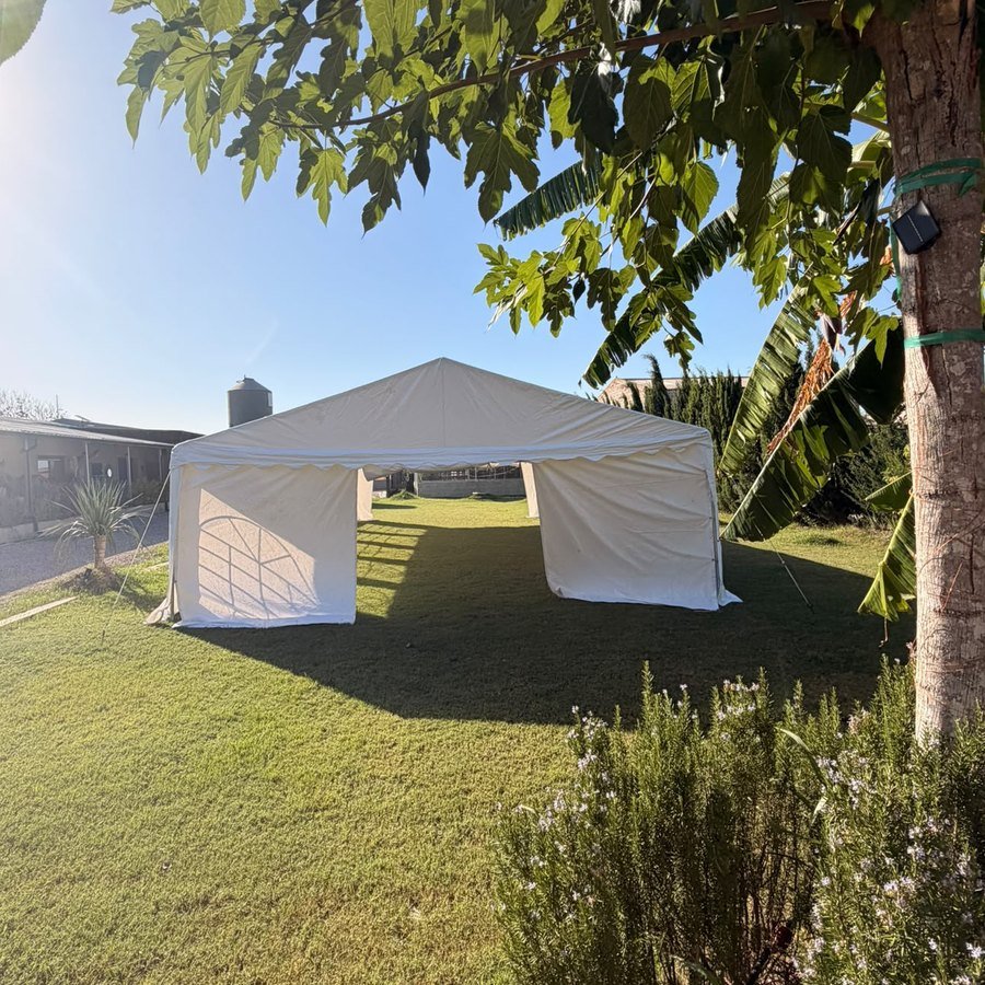Carpa blanca montada sobre el césped del jardín, a la sombra de los árboles, en Knattur