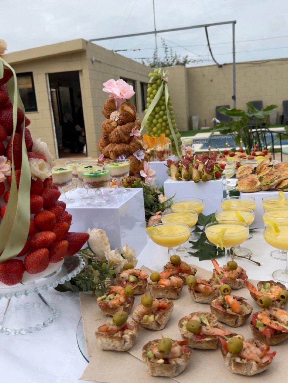 Mesa de brunch mediterráneo con frutas, bollería y cócteles junto a la piscina