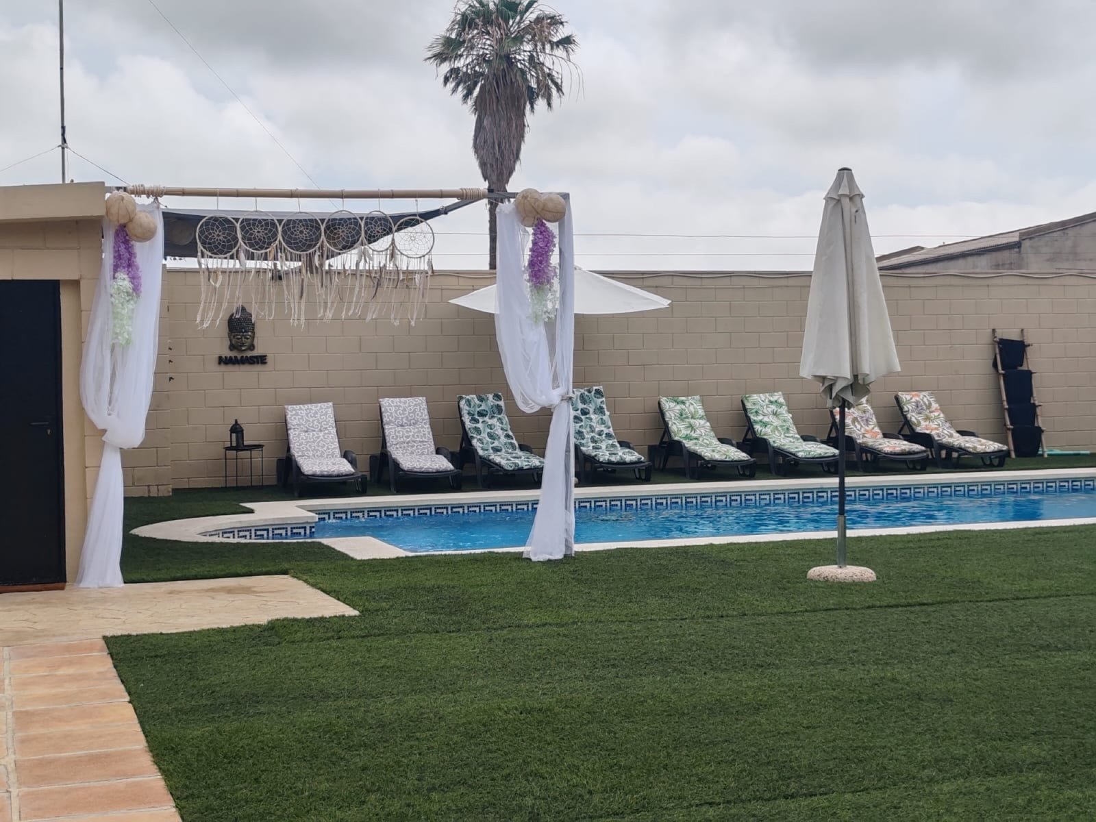 Piscina con arco boho y palmeras al sol