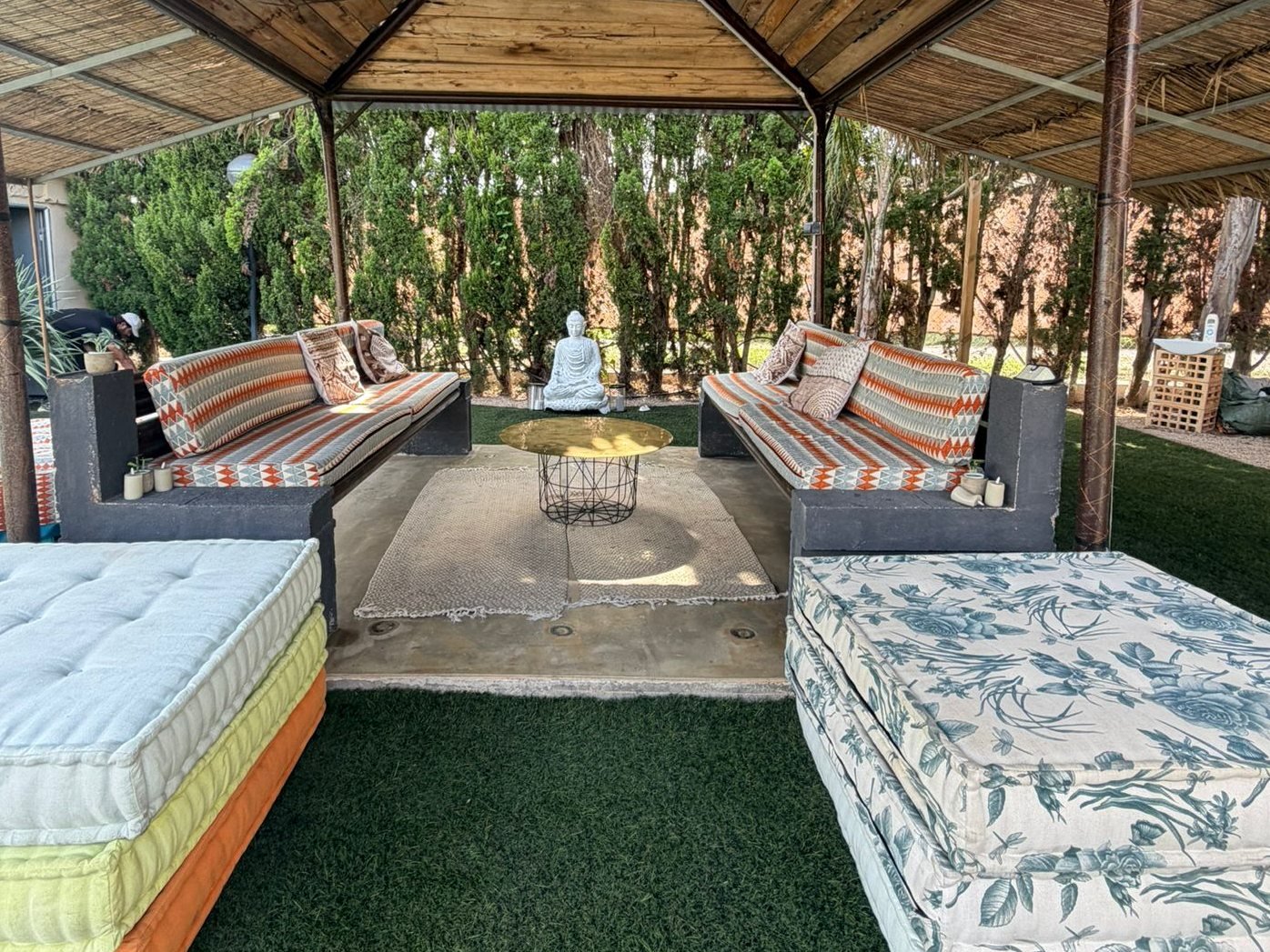 Zona chill-out bajo palapa de cañizo con bancos boho, colchonetas y figura de Buda