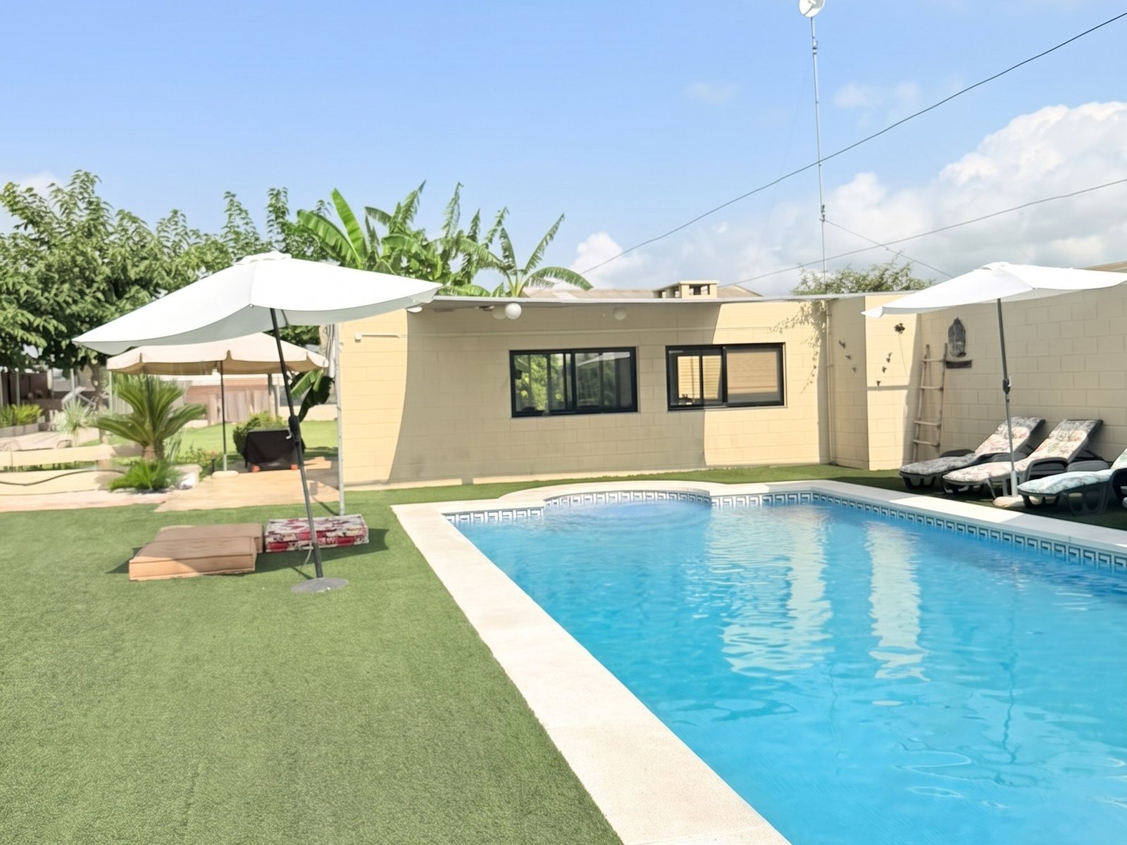 Piscina de la finca Knattur al sol, con el jardín, las sombrillas y las hamacas