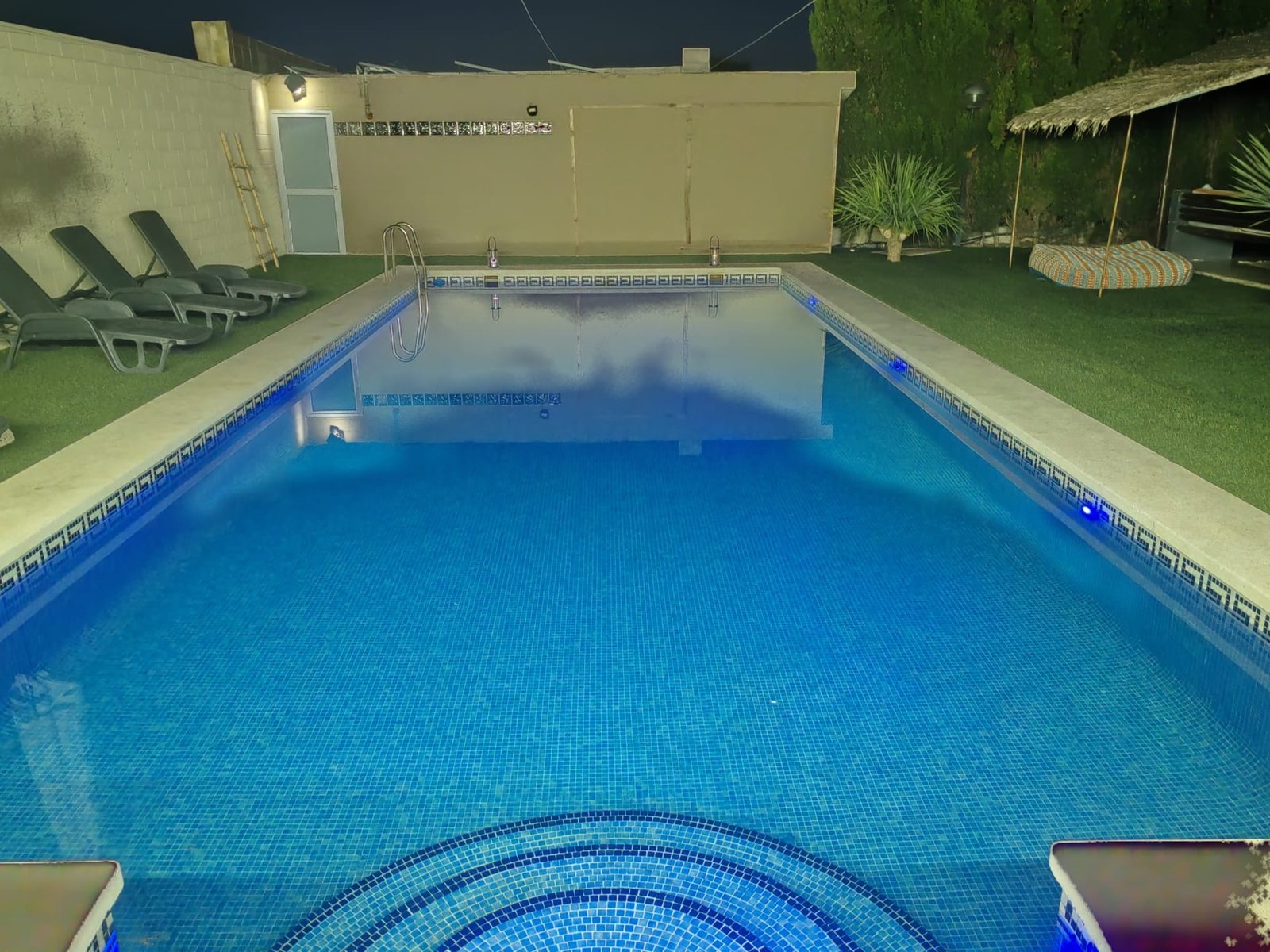 Piscina iluminada al anochecer bajo la palapa
