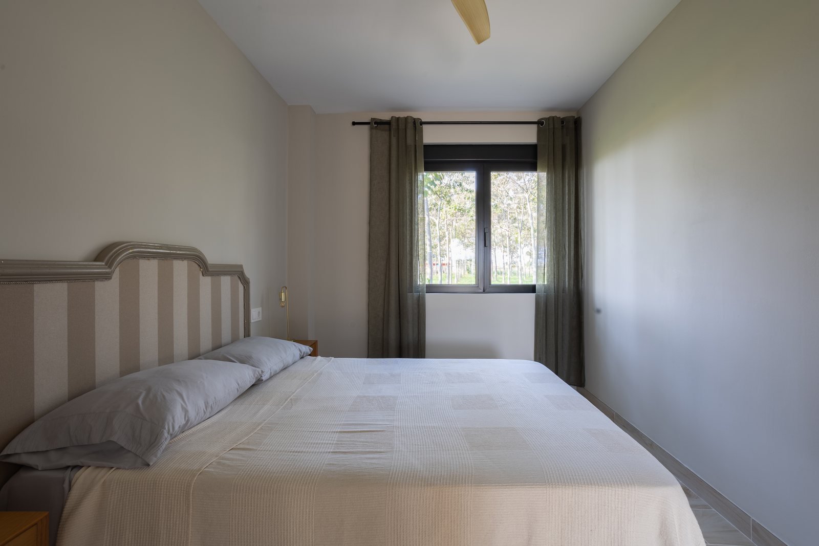 Dormitorio principal del apartamento Río con cabecero de rayas y ventana al bosque